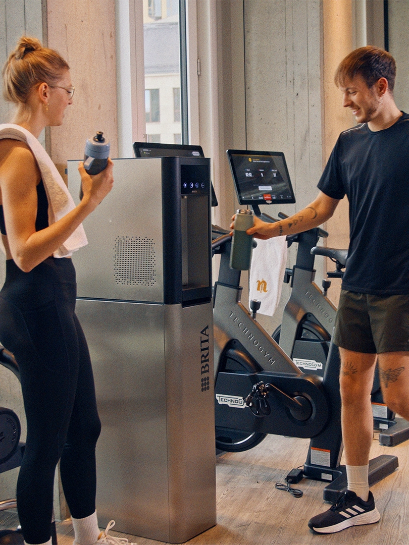 Two people using BRITA water dispenser in gym.