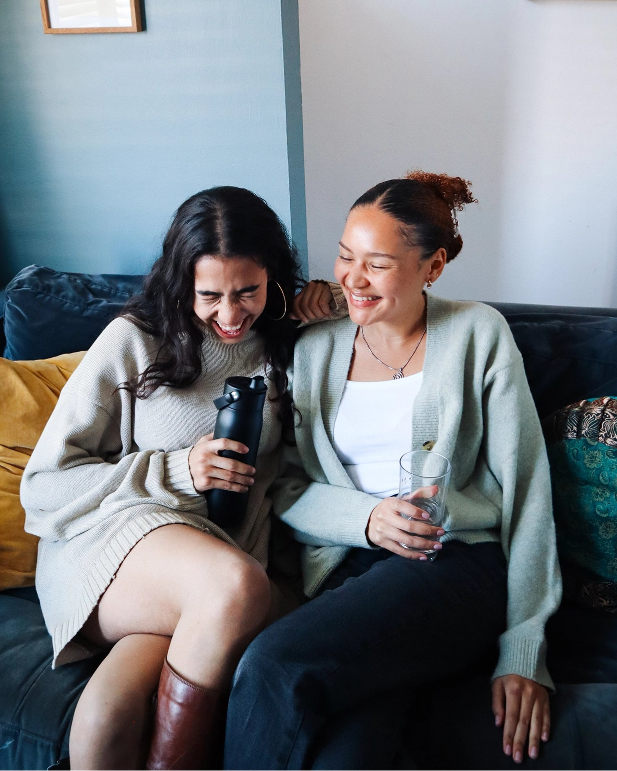 Two girls laughing and sitting on a couch with black BRITA LARQ water filter bottle.
