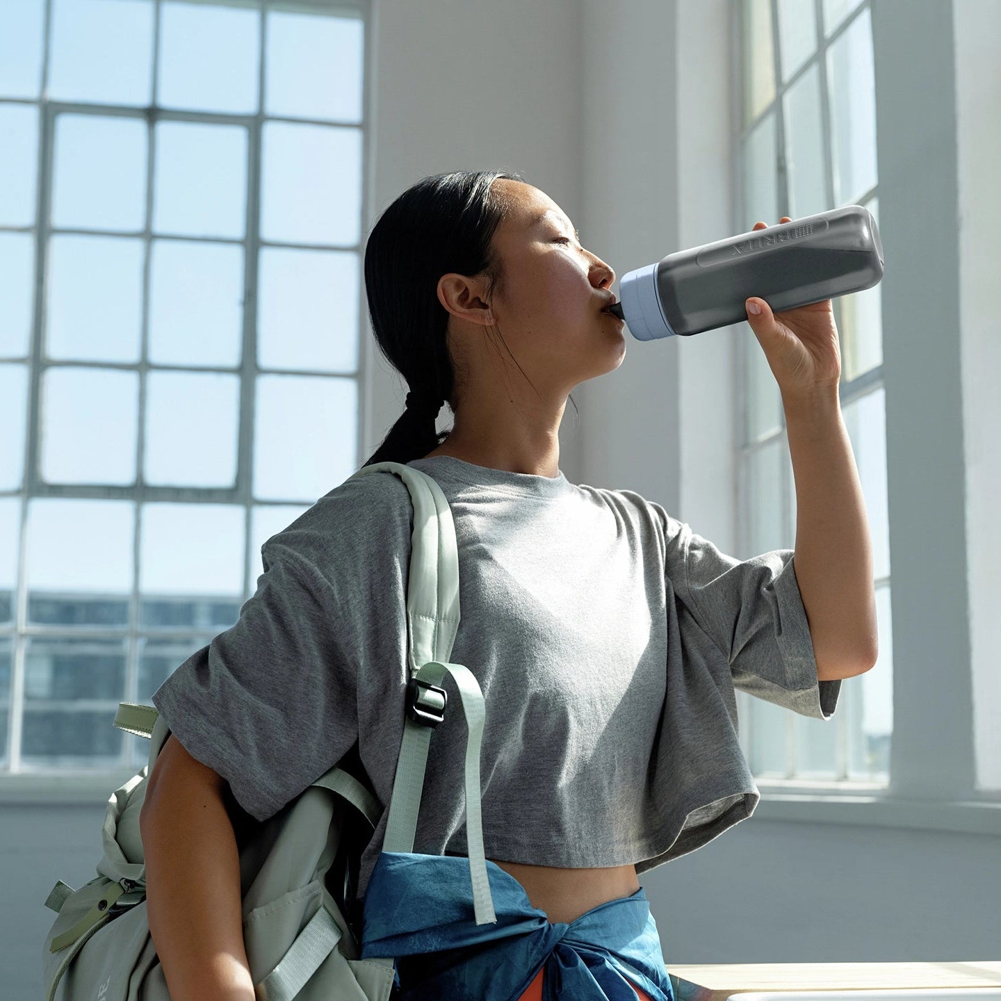 Vrouw die uit een BRITA-waterfles drinkt filter Flesmodel in een lichte kamer met grote ramen.