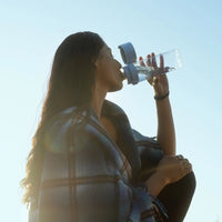 Person drinking from BRITA water filter bottle Model Vital against a clear blue sky