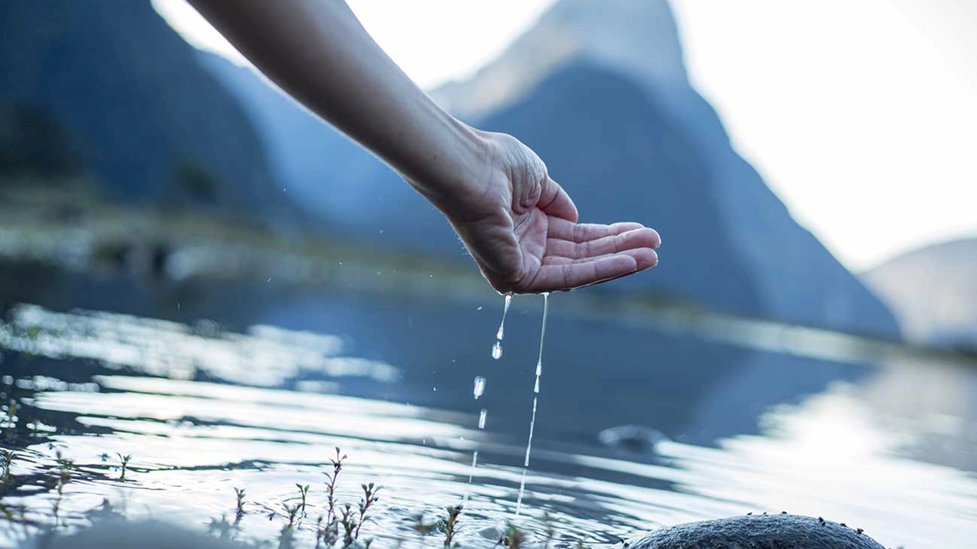 Hand scooping water out of a river with mountains in the background.