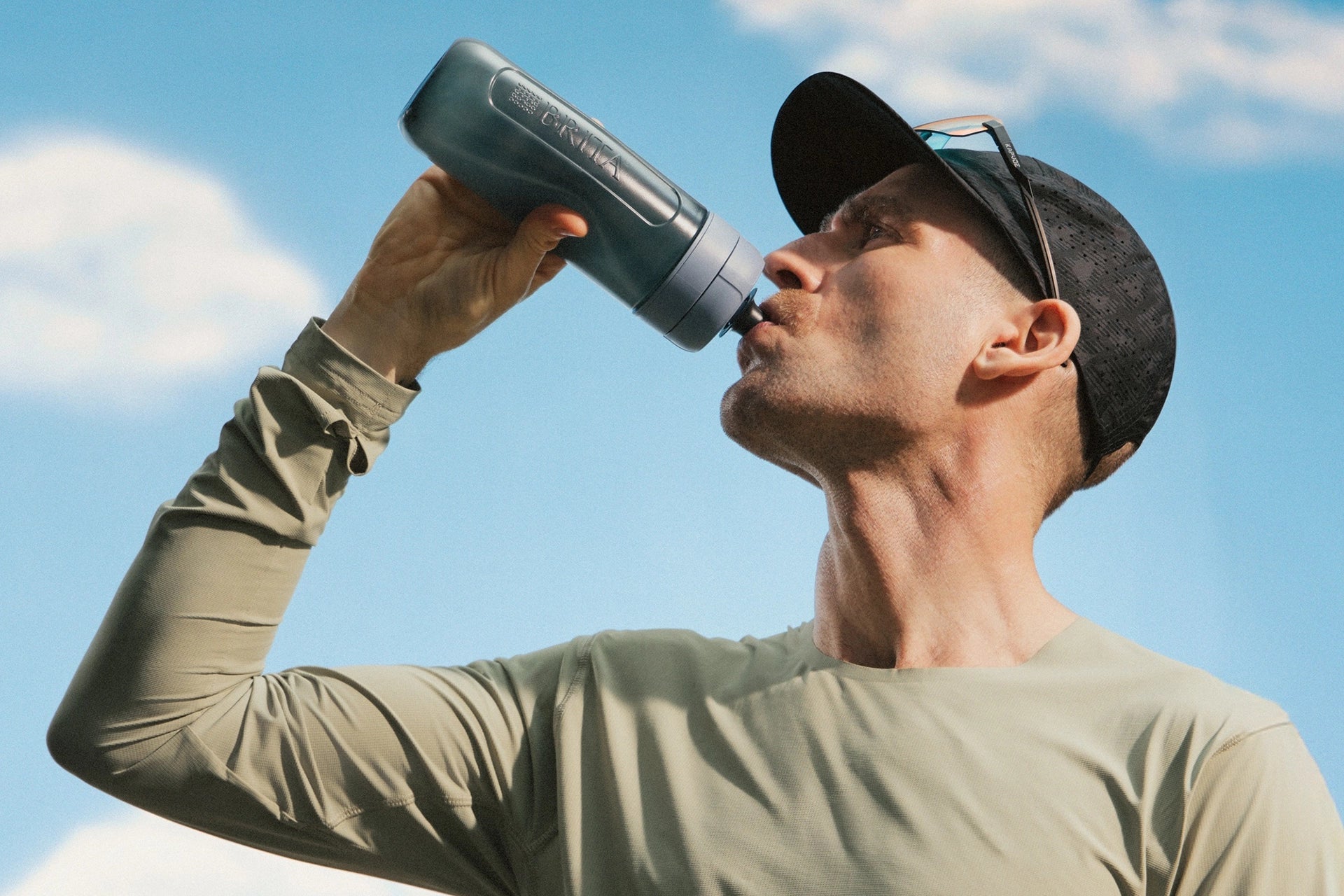 Man drinking from a BRITA water filter bottle against a blue sky.