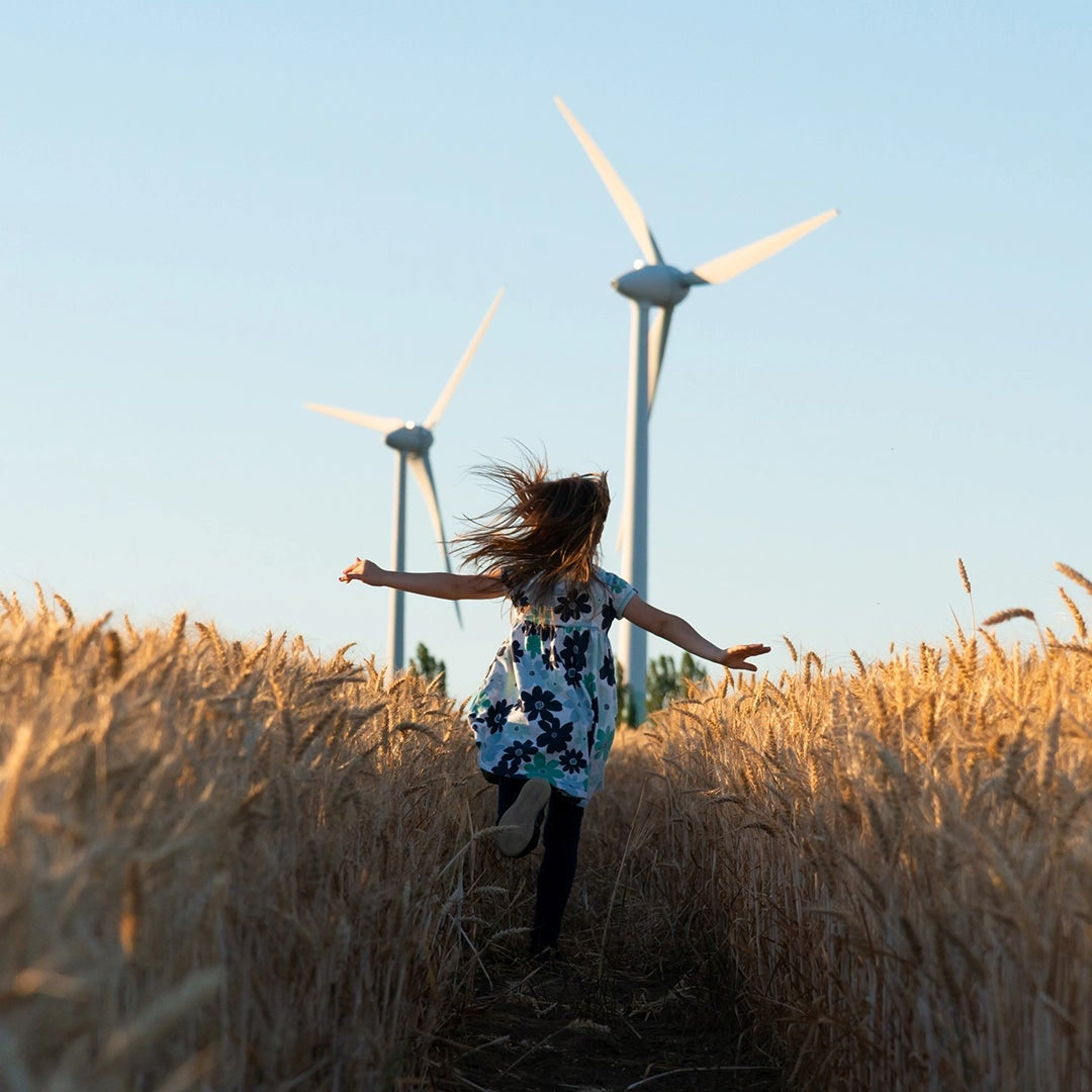Girl running through a field of grass with wind turbines in the background.