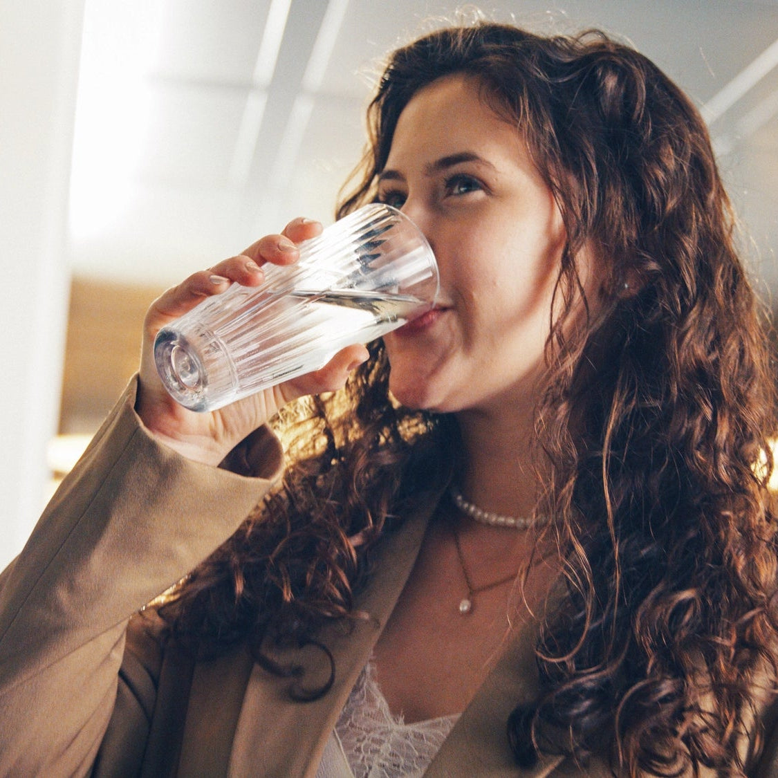 Une femme en train de boire de l'eau à l'intérieur, avec un arrière-plan flou