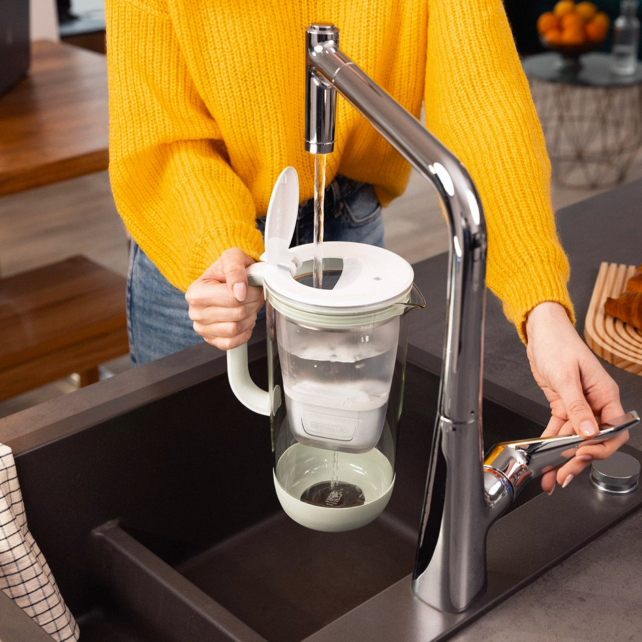 Person filling a green BRITA Glass Jug with tap water at a kitchen sink.