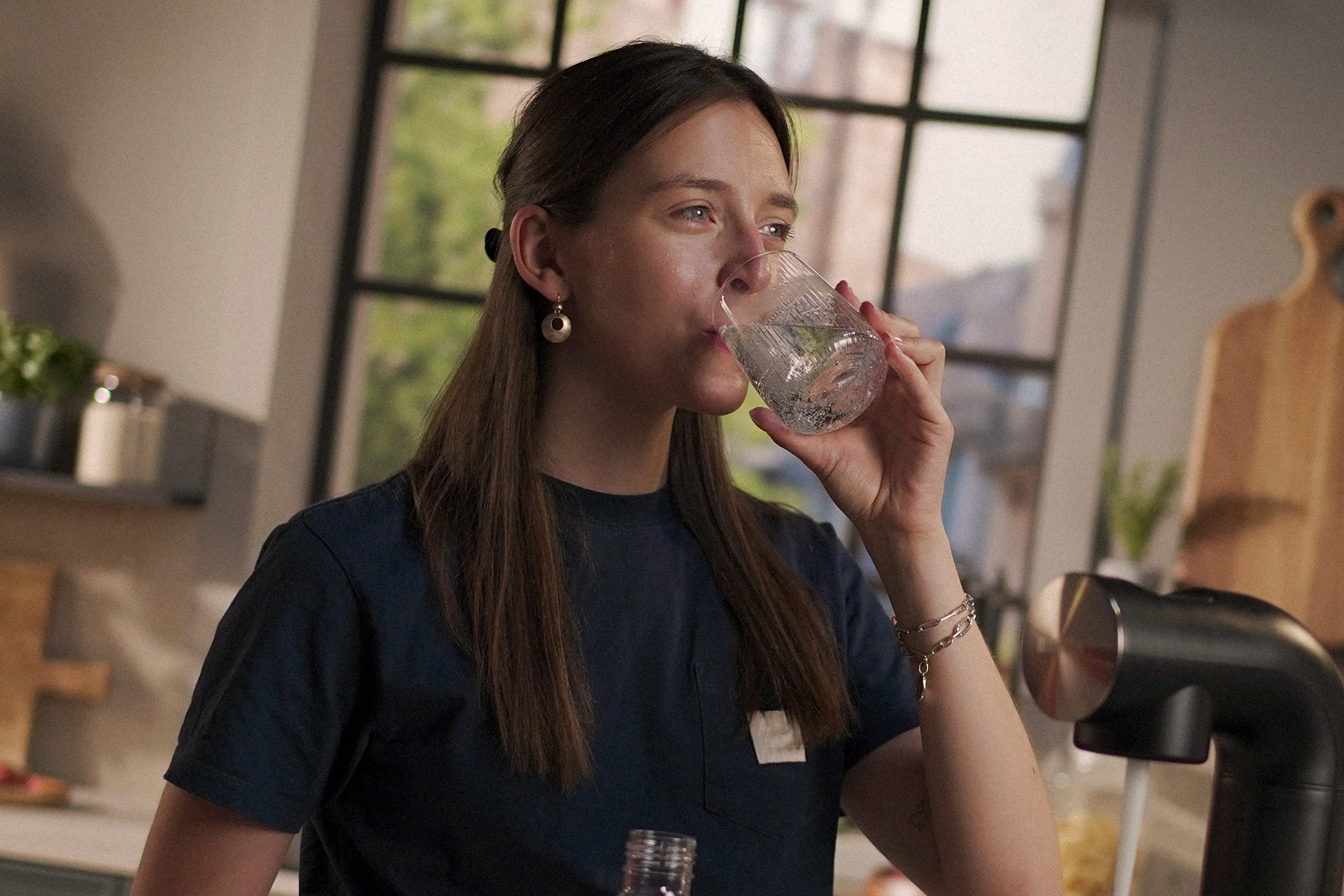 Woman drinking a glass of sparkling water in a kitchen setting