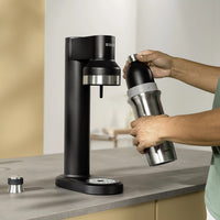 Person inserting a BRITA sodaTRIO Stainless Steel Bottle into a black BRITA sodaTRIO Sparkling Water Maker.