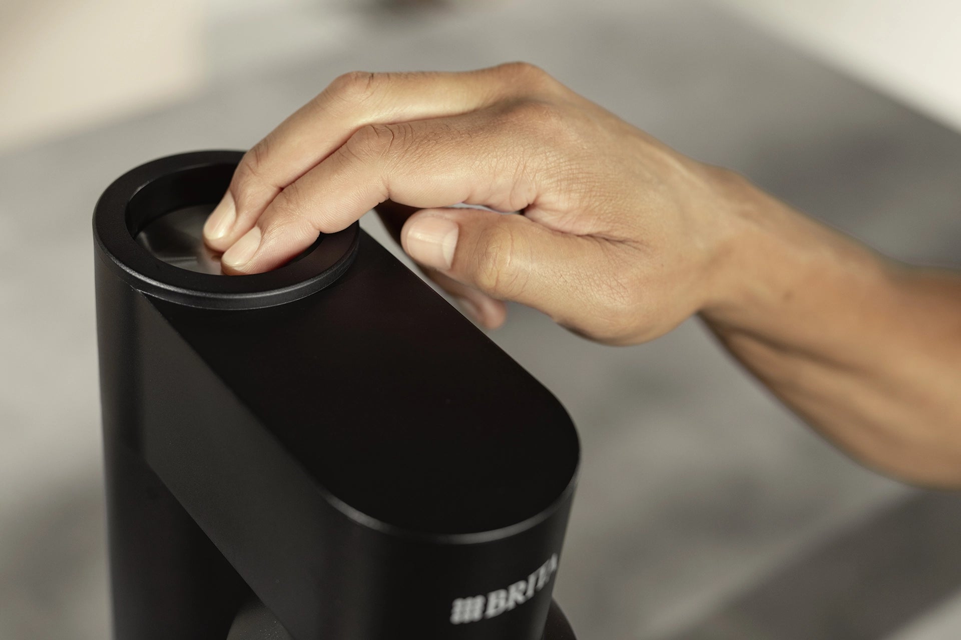 Person pressing the carbonation button on a black BRITA sodaTRIO Sparkling Water Maker.