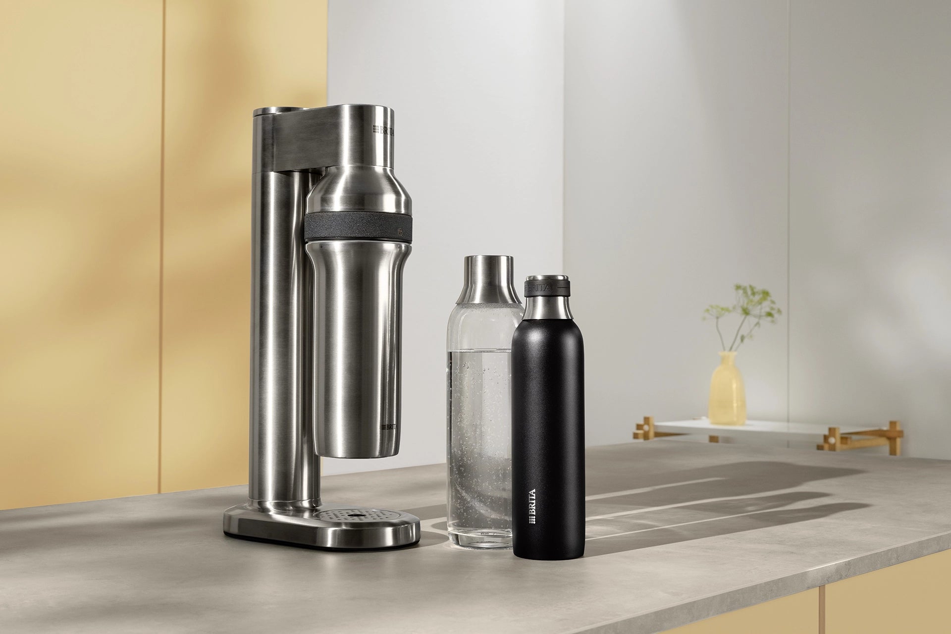 BRITA sodaTRIO Pro Sparkling Water Maker displayed with a BRITA sodaTRIO Glass Bottle and a BRITA sodaTRIO Stainless Steel Bottle on a countertop
