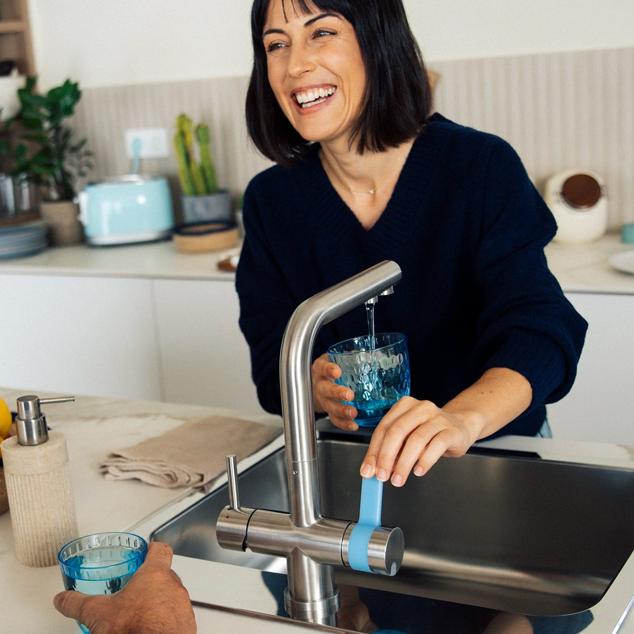 Woman pouring water from BRITA 3-way water filter tap into a glass in a kitchen with a man standing next to her.