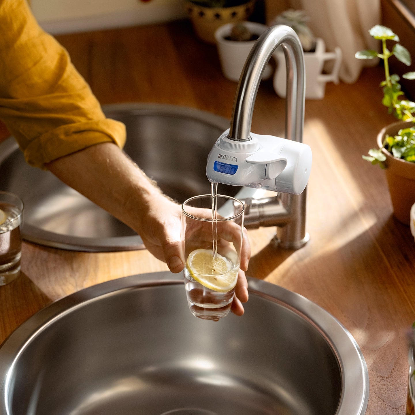 Glass with a lemon slice being filled with filtered water from a BRITA ON TAP Pro water filter system.
