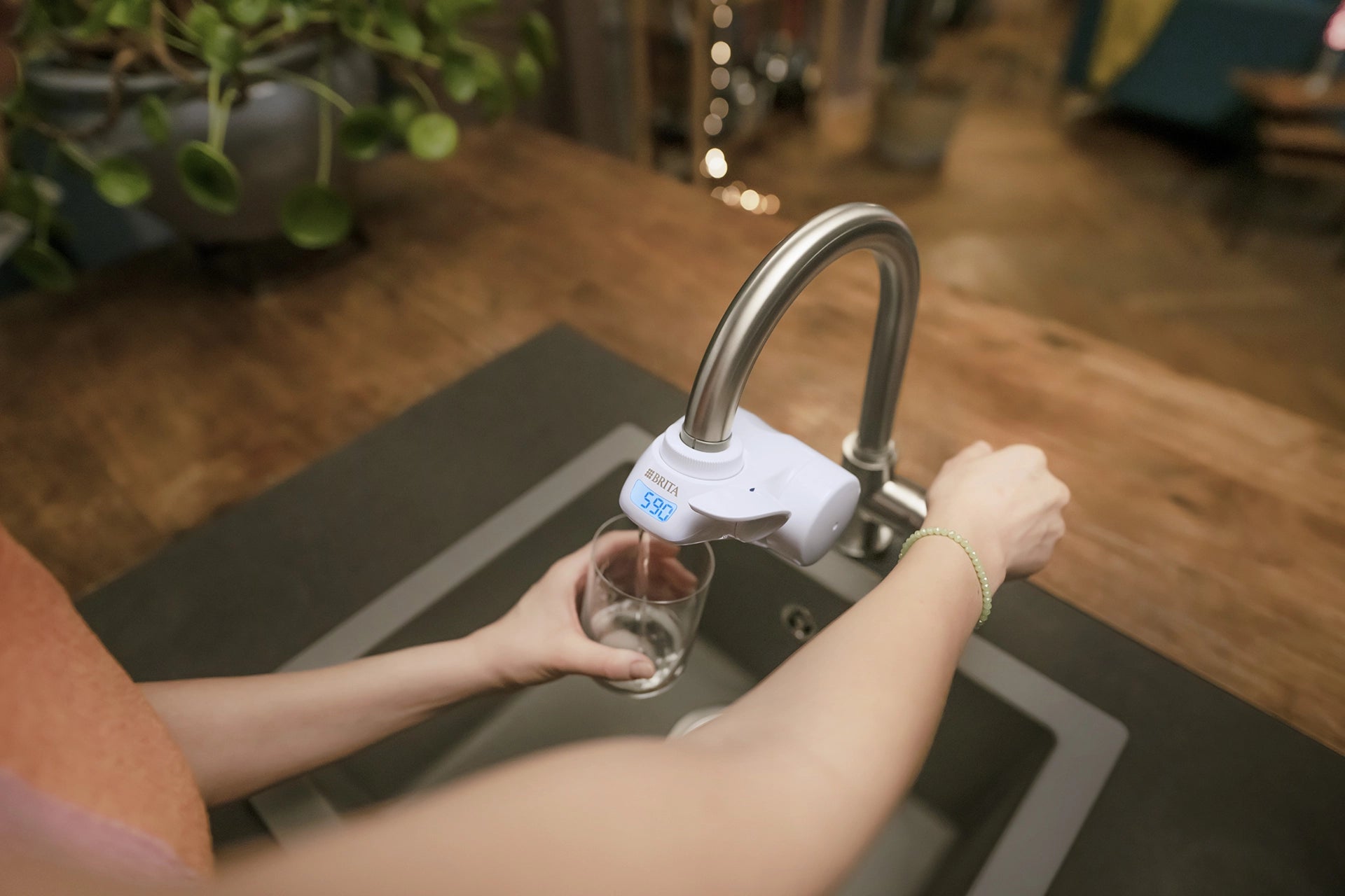 Person filling a glass with filtered water from a BRITA ON TAP Pro water filter.